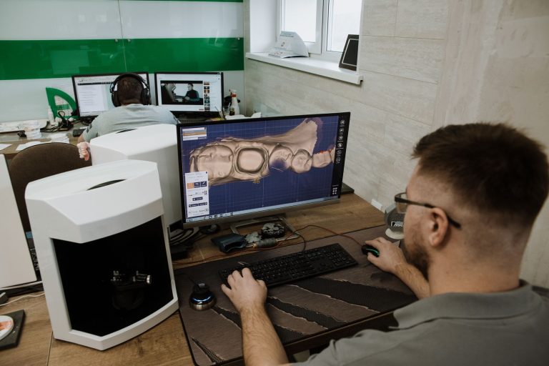 SUS amplia uso de próteses dentárias digitais com oficinas em todas as regiões do Brasil Profissional visto de costas trabalhando na criação de um modelo 3D de dentes em um laboratório odontológico moderno