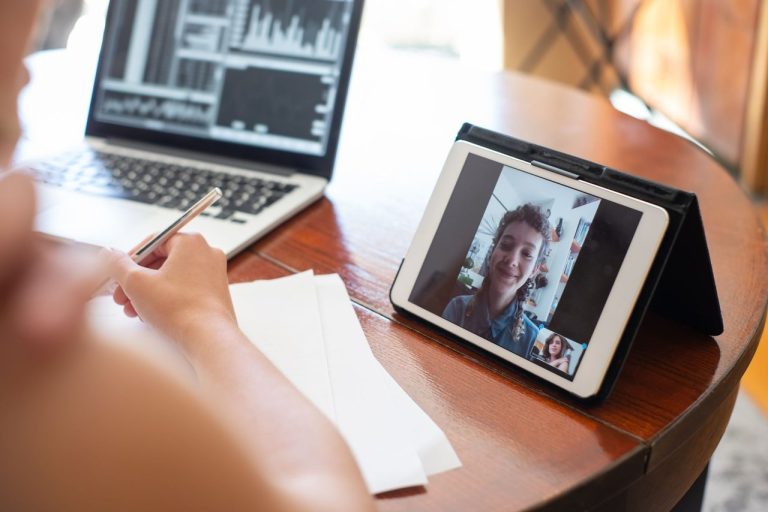 Antes de transferir dinheiro, Interpol pede checagem contra falsificações de voz e rosto Pessoa participa de uma videochamada em um tablet, com um laptop exibindo dados ao lado.