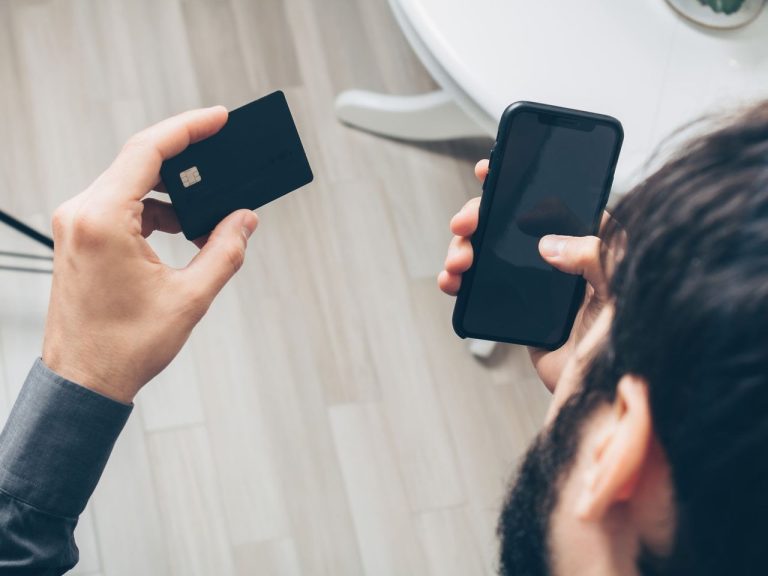 Pagamento online exige conferência do recebedor antes da confirmação do Pix Homem segura um smartphone e um cartão enquanto realiza um pagamento online em ambiente interno.
